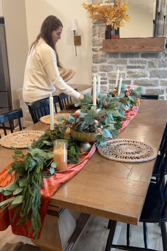 Setting round woven placemats around the table beside the greenery and candles